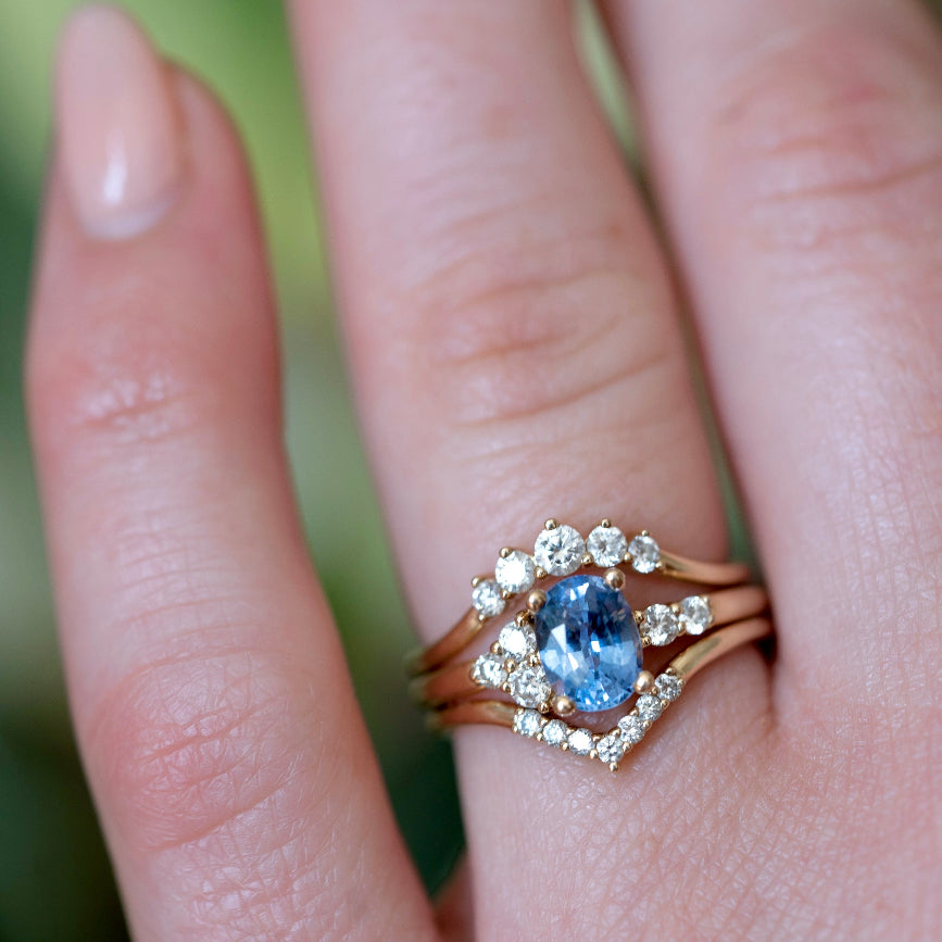 A close-up of a hand wearing a gold ring with a ceylon sapphire stone and surrounding asymmetrical round diamonds. 